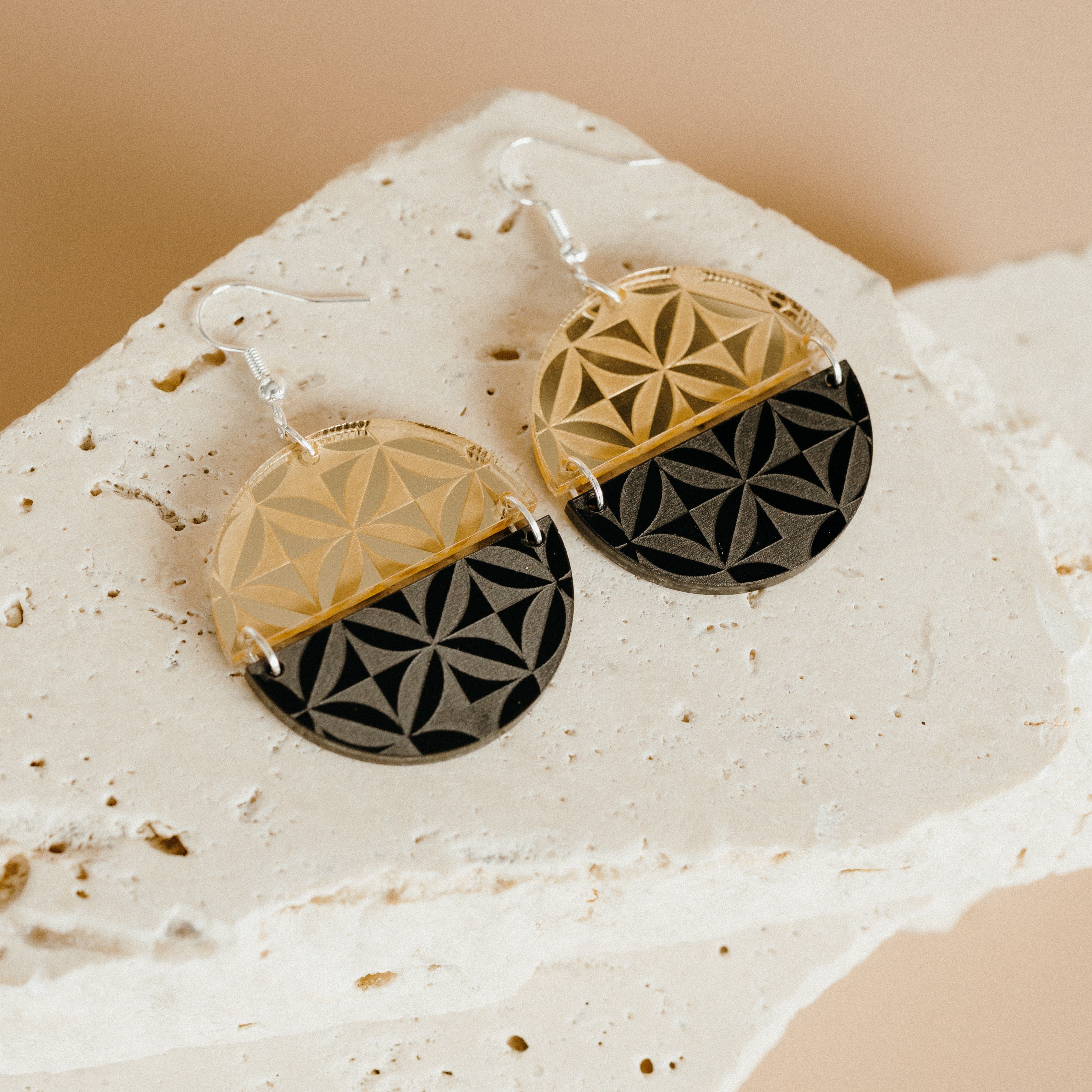 Manulua Symmetry earrings on textured stone; gold mirror acrylic top with black base.
