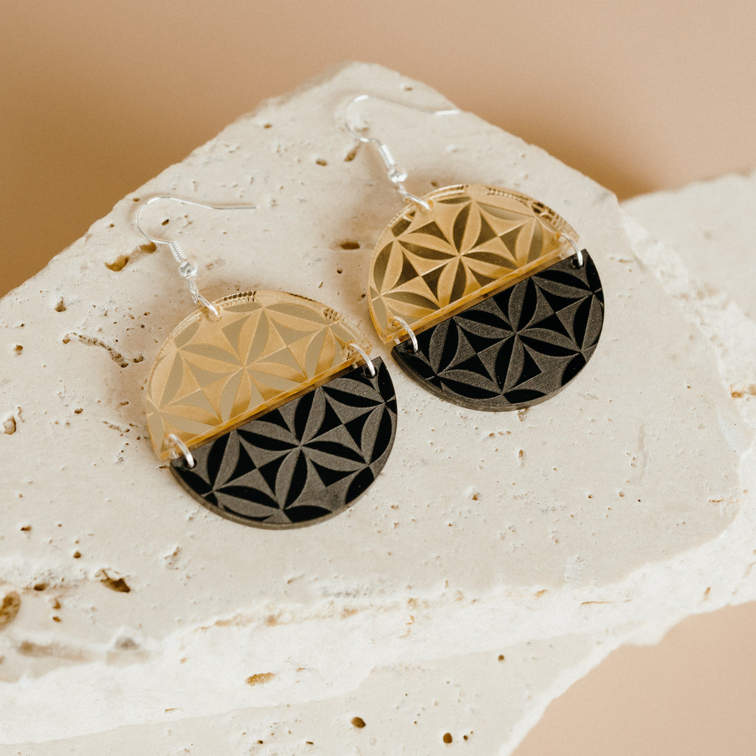 Manulua Symmetry earrings on textured stone; gold mirror acrylic top with black base.