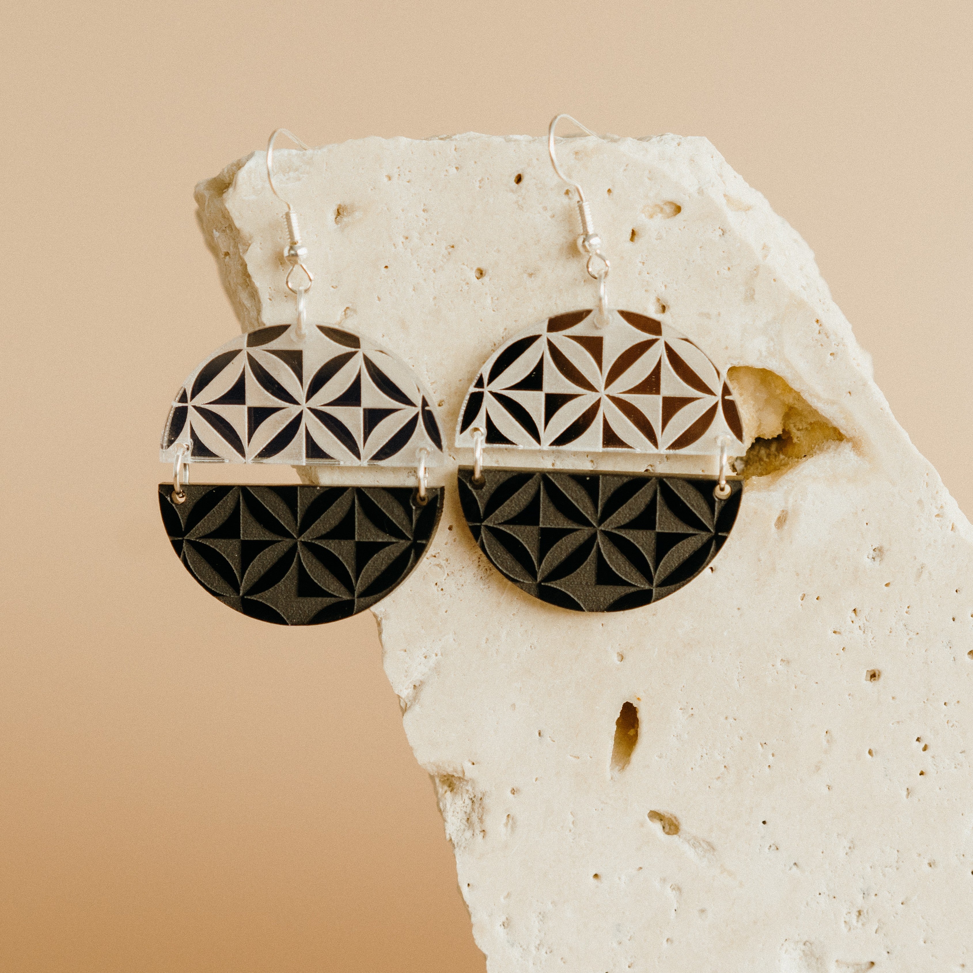 Manulua Symmetry earrings on textured stone; silver mirror acrylic top with black base.