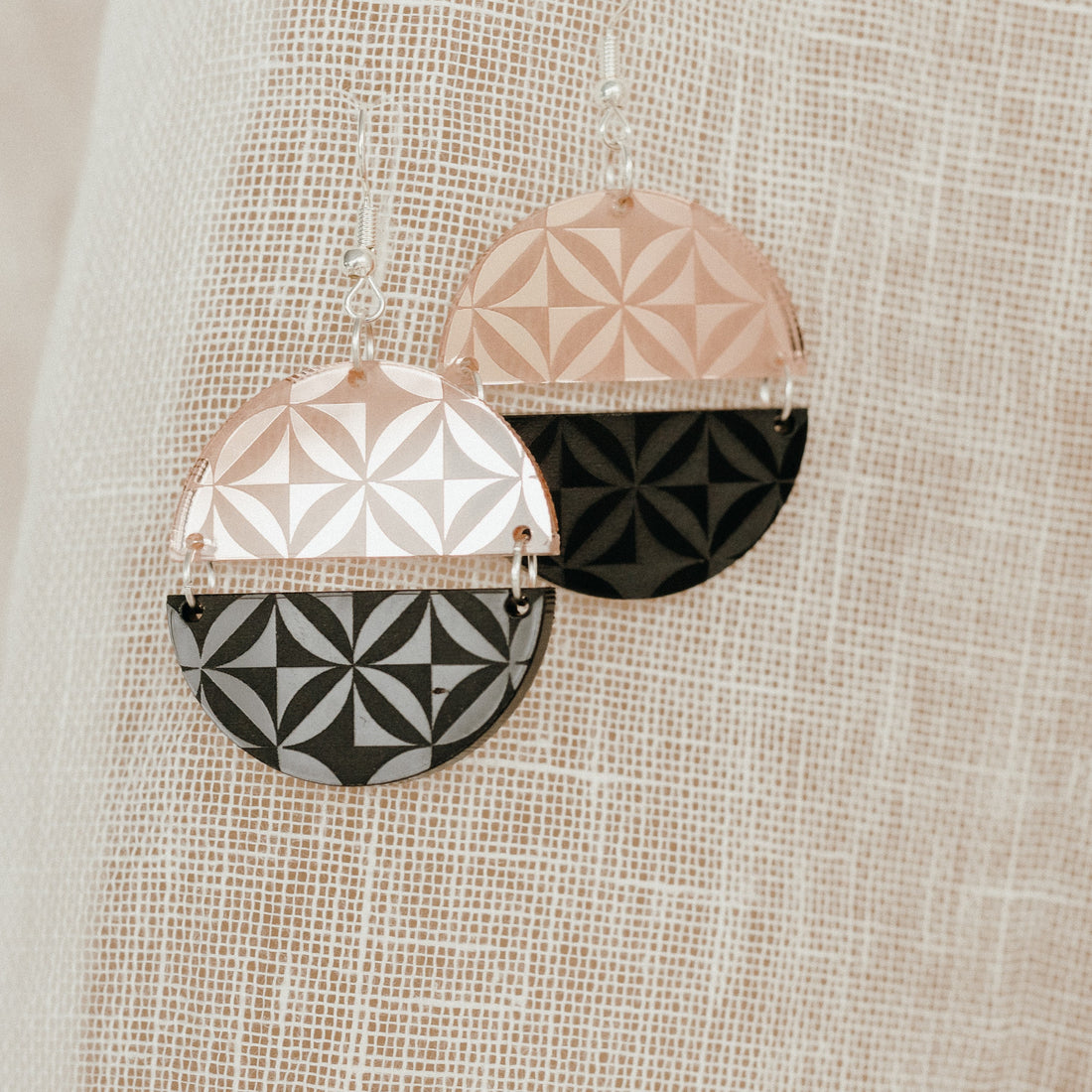 Manulua Symmetry earrings on woven fabric; rose-gold mirror–black and silver mirror–black pairs.