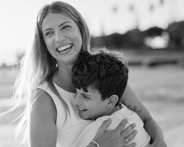 Black and white photo of a woman and a child embracing on a beach.