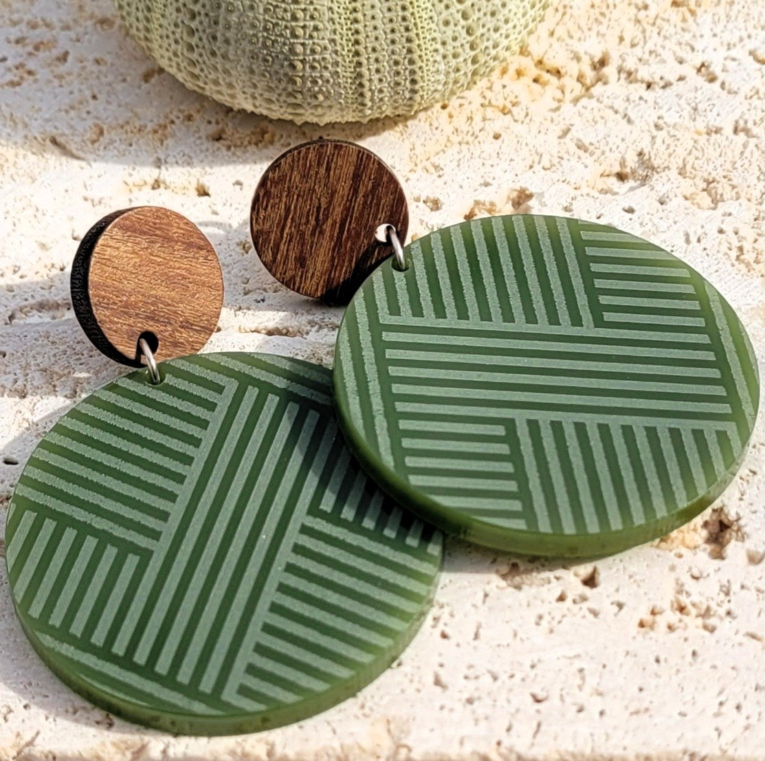 Mana Wood Stud earrings styled on coral with a sea urchin; natural wood studs above Pounamu Satin Acrylic woven discs.