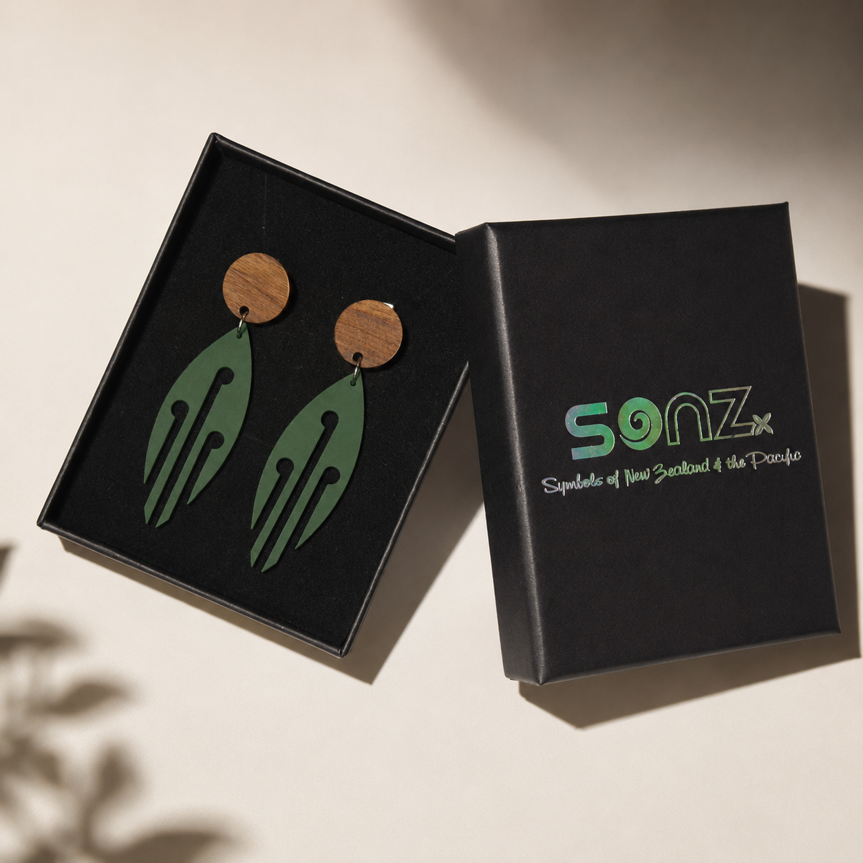 Ponga Wood Stud earrings in Pounamu Satin Acrylic presented in an open SONZ gift box in a professional studio setting.